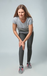 Full length portrait of sportswoman having knee problems on grey background