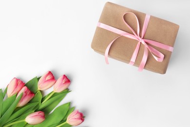 Beautiful gift box with bow and pink tulips on white background, flat lay. Space for text