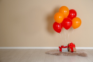 Bunch of bright balloons and gifts on floor against color wall. Space for text