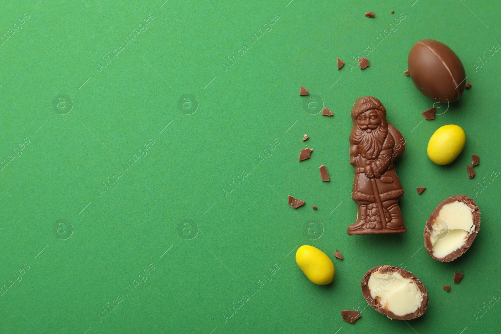 Photo of Chocolate Santa Claus candy and sweets on green background, flat lay. Space for text