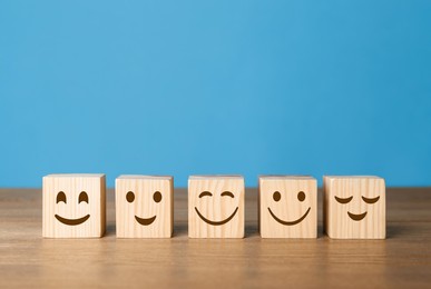 Image of Cubes with different emoticons in row on wooden table against light blue background