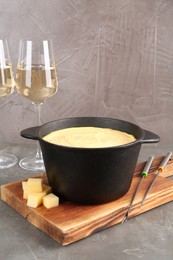 Fondue pot with tasty melted cheese, forks and wine on grey table