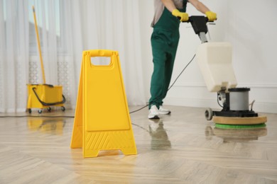 Photo of Professional janitor cleaning parquet floor with polishing machine indoors, closeup
