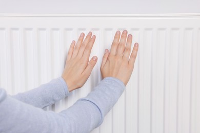 Photo of Woman warming hands on heating radiator, closeup