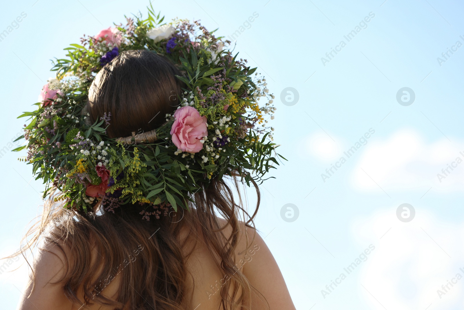 Photo of Young woman wearing wreath made of beautiful flowers outdoors on sunny day, back view