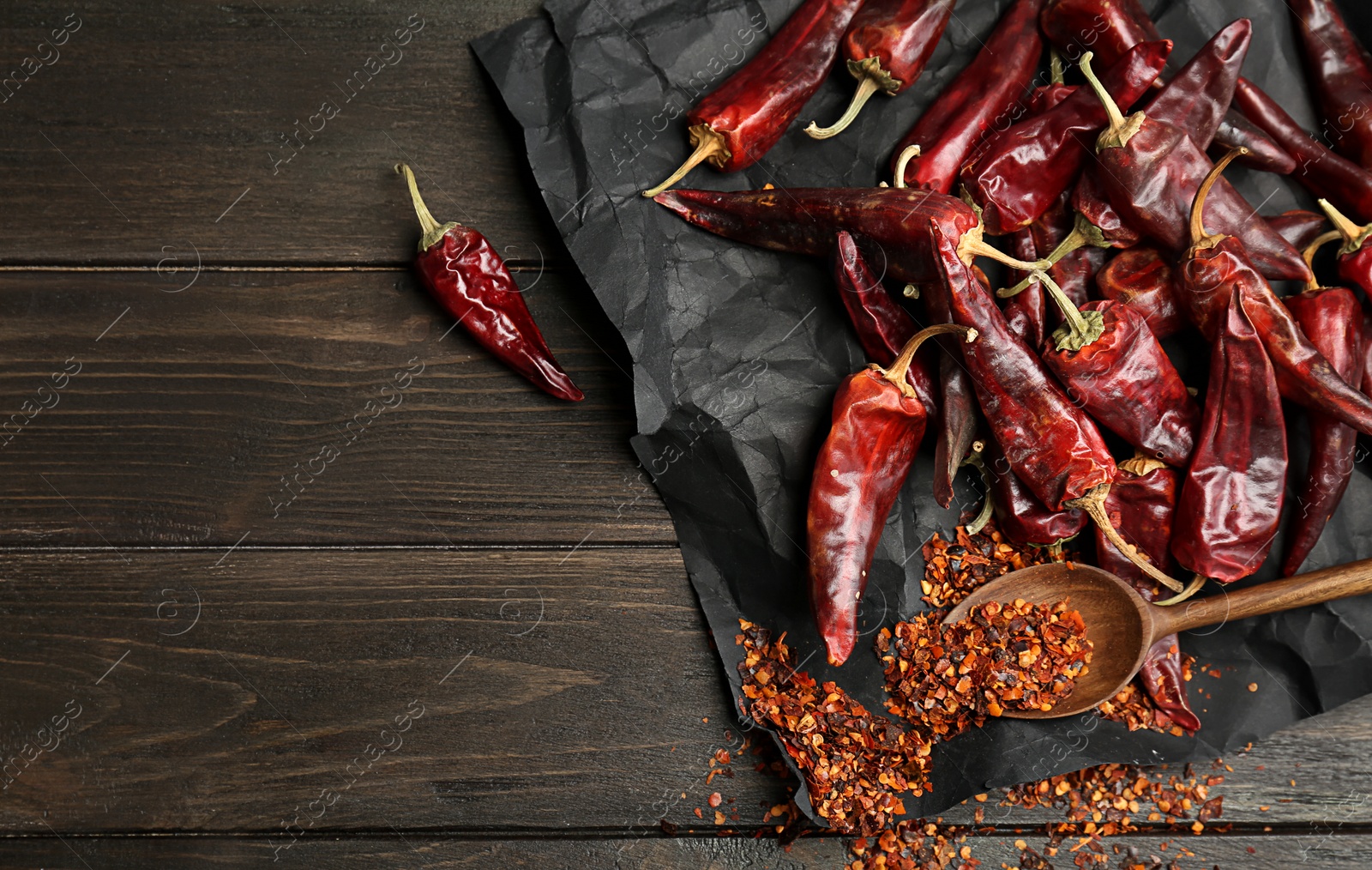 Photo of Spoon with chili pepper powder and pods on wooden table