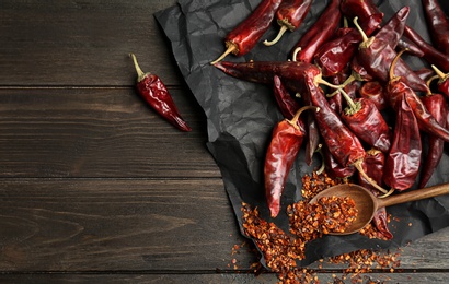 Photo of Spoon with chili pepper powder and pods on wooden table