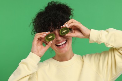 Photo of Woman covering eyes with halves of kiwi on green background