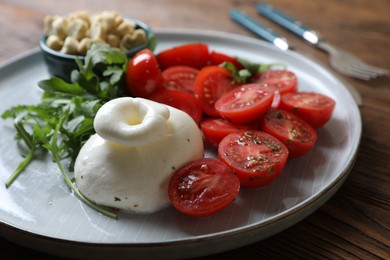 Photo of Delicious burrata cheese with tomatoes and arugula served on wooden table, closeup