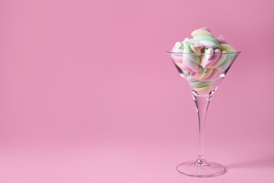 Photo of Beautiful martini glass with colorful marshmallows on pink background. Space for text