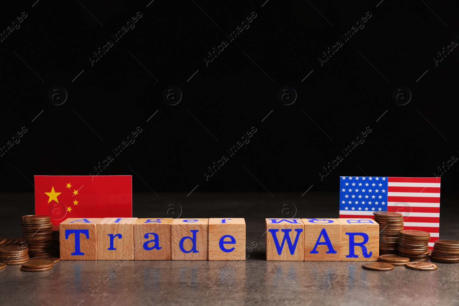 Photo of Words Trade War made of wooden cubes, American and Chinese flags with coins on grey table