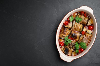 Tasty eggplant rolls with tomatoes, cheese and parsley in baking dish on black table, top view. Space for text