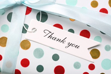 Photo of White tag with phrase Thank You on gift box, closeup