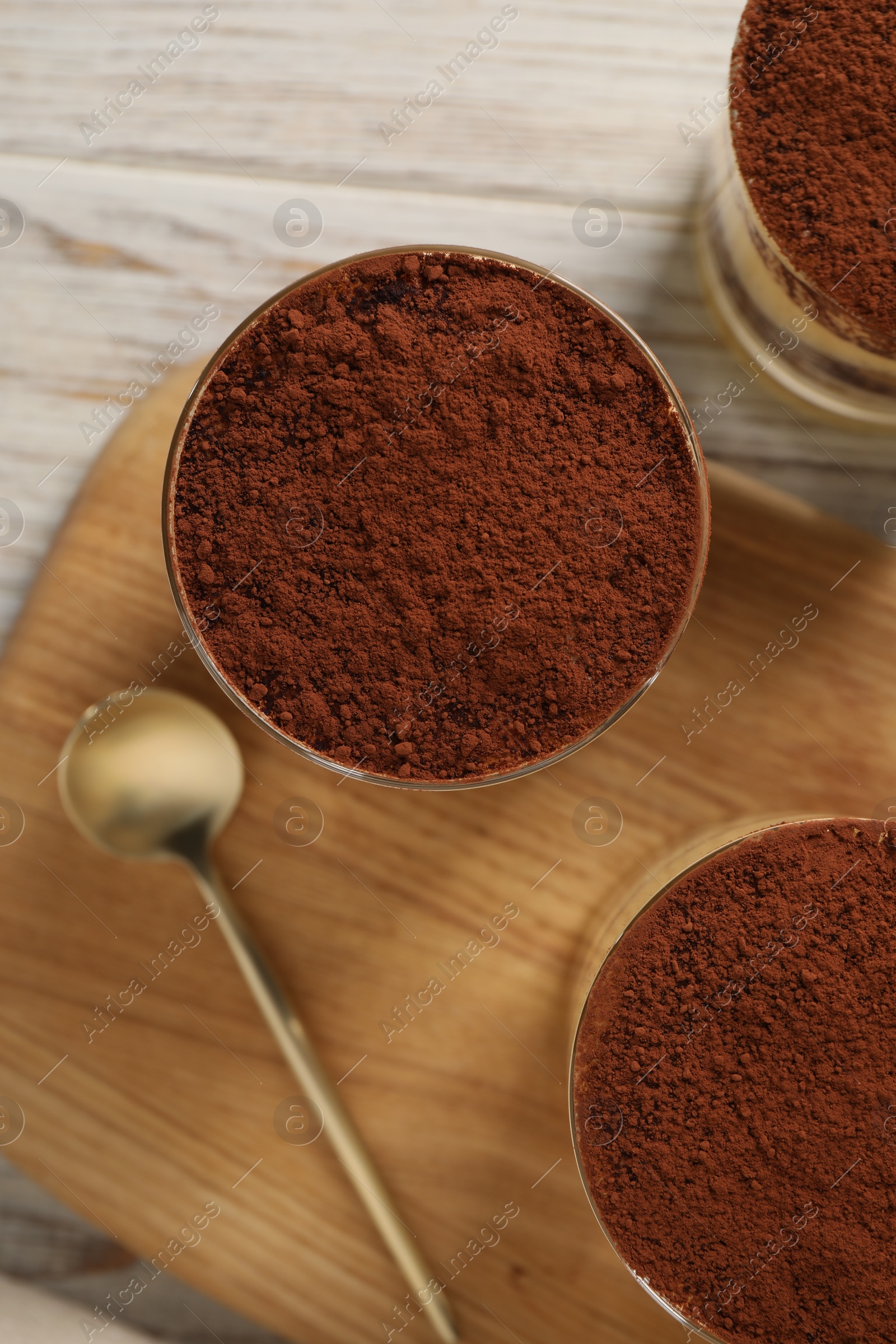 Photo of Delicious tiramisu in glasses and spoon on light wooden table, top view