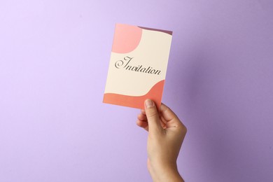 Photo of Woman holding beautiful card with word Invitation on lilac background, closeup
