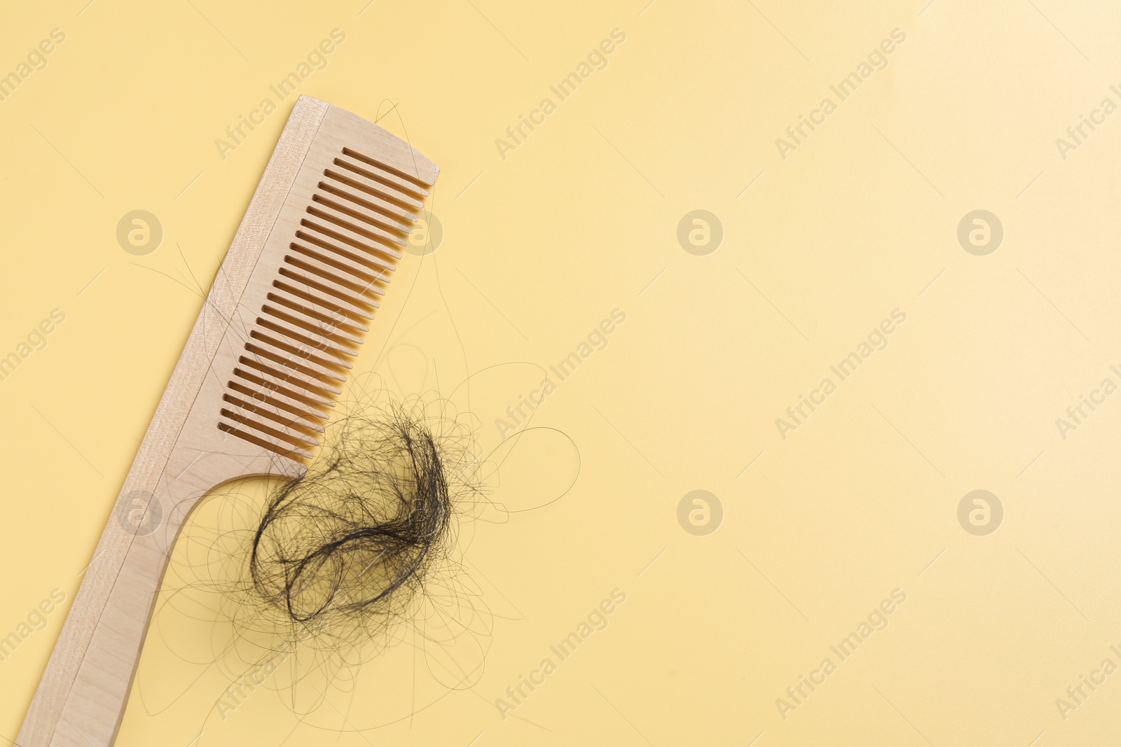 Photo of Wooden comb with lost hair on yellow background, top view. Space for text