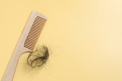 Photo of Wooden comb with lost hair on yellow background, top view. Space for text