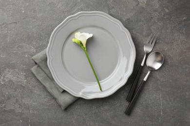 Stylish setting with cutlery, napkin, flower and plate on grey textured table, flat lay