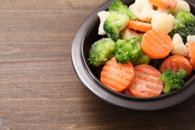 Photo of Mix of different frozen vegetables in bowl on wooden table, closeup. Space for text
