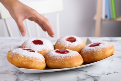 Photo of Woman taking Hanukkah doughnut with jelly and sugar powder at white marble table indoors, closeup