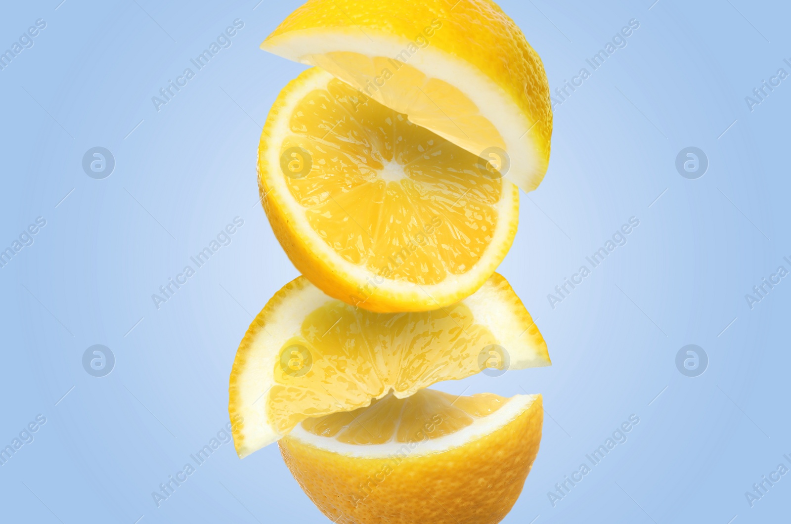 Image of Cut fresh lemons falling on light blue background