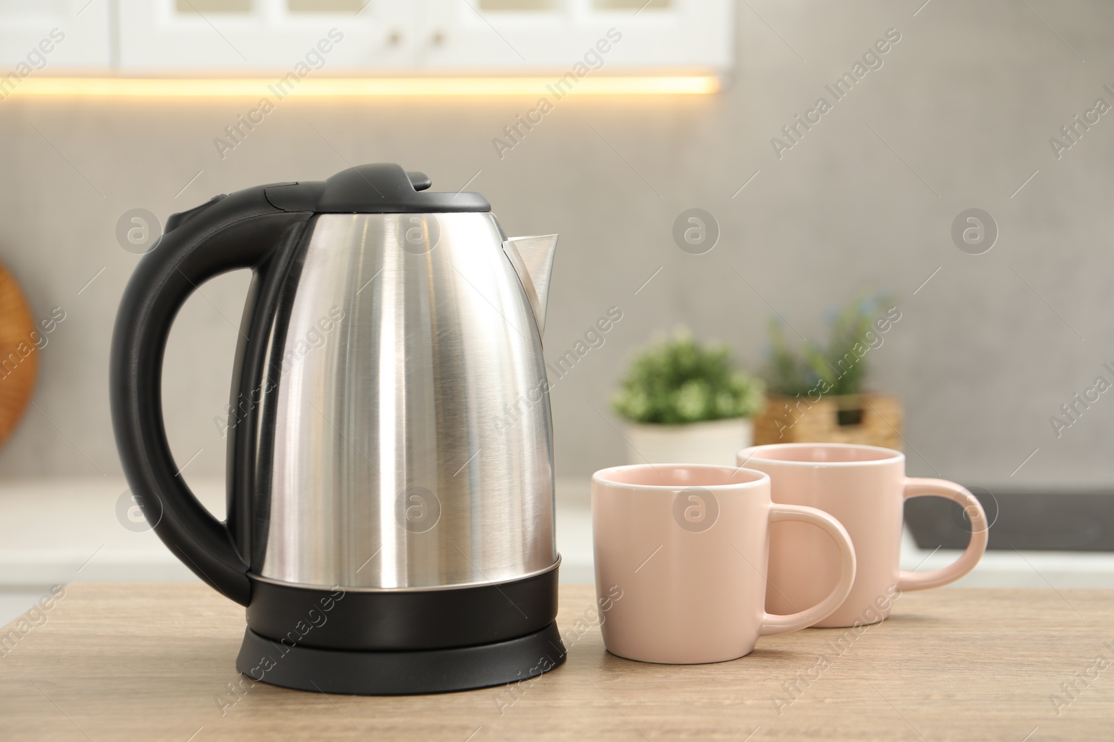 Photo of Modern electric kettle and cups on table in kitchen. Space for text