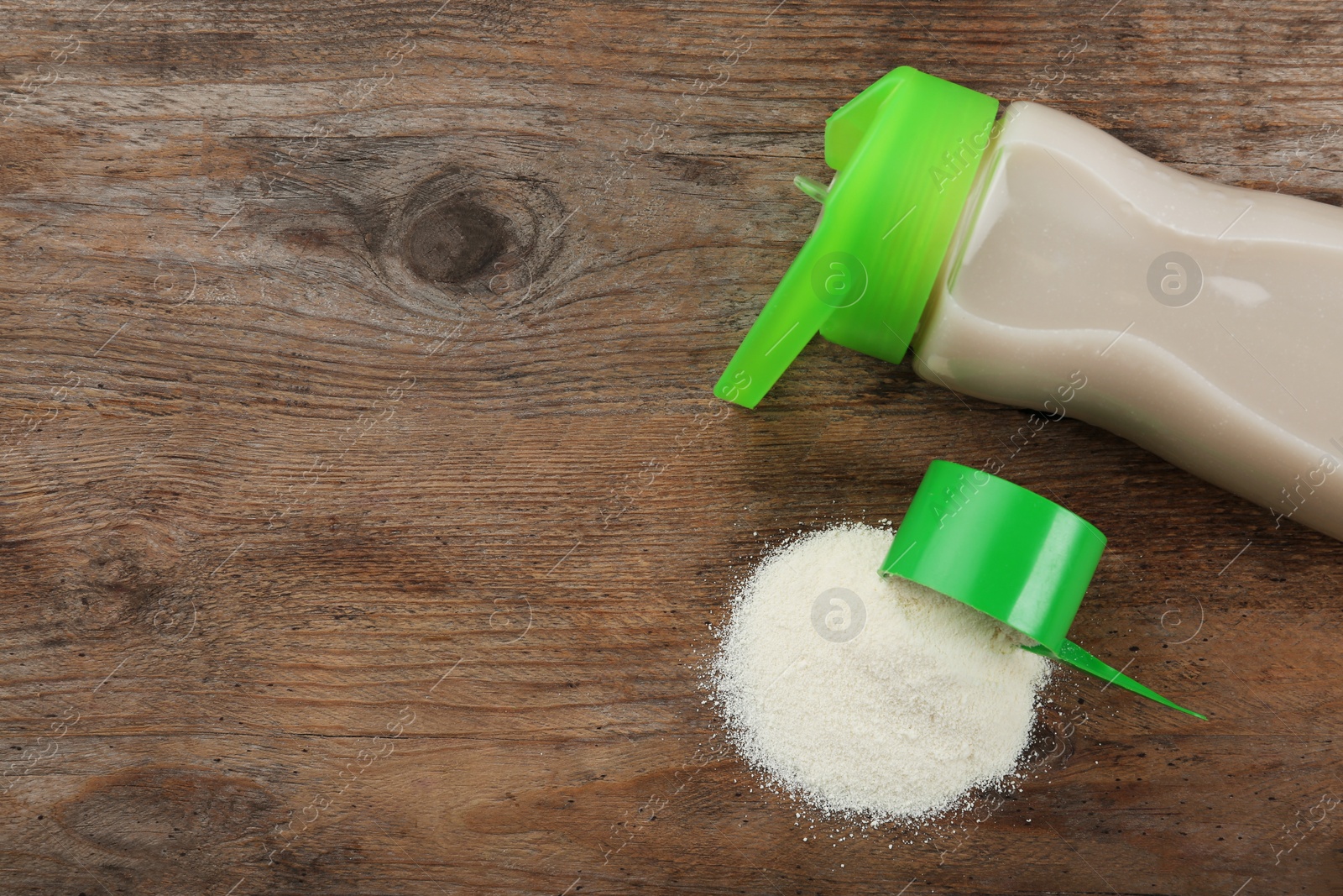 Photo of Measuring scoop of protein powder and bottle with shake on wooden table, flat lay. Space for text