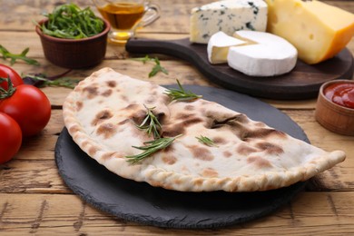 Photo of Delicious calzone and products on wooden table