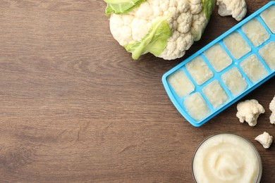 Cauliflower puree in ice cube tray and fresh cauliflower on wooden table, flat lay. Space for text