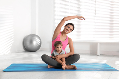 Young woman doing exercise with her son indoors. Home fitness