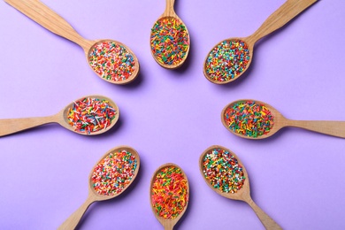 Photo of Colorful sprinkles in spoons on lilac background, flat lay with space for text. Confectionery decor