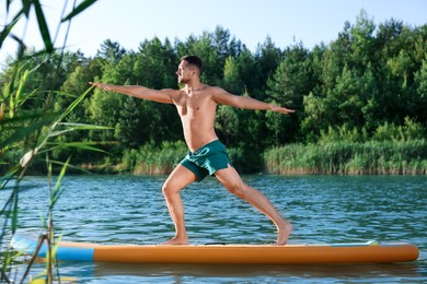 Photo of Man practicing yoga on color SUP board on river