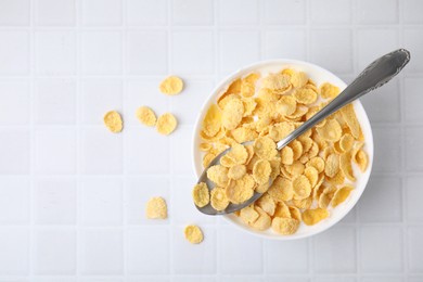 Photo of Breakfast cereal. Tasty corn flakes with milk in bowl and spoon on white tiled table, top view. Space for text