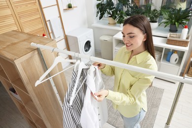 Photo of Happy young woman taking shirt from rack in laundry room, above view