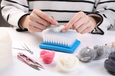 Photo of Woman felting toy from wool at white wooden table, closeup