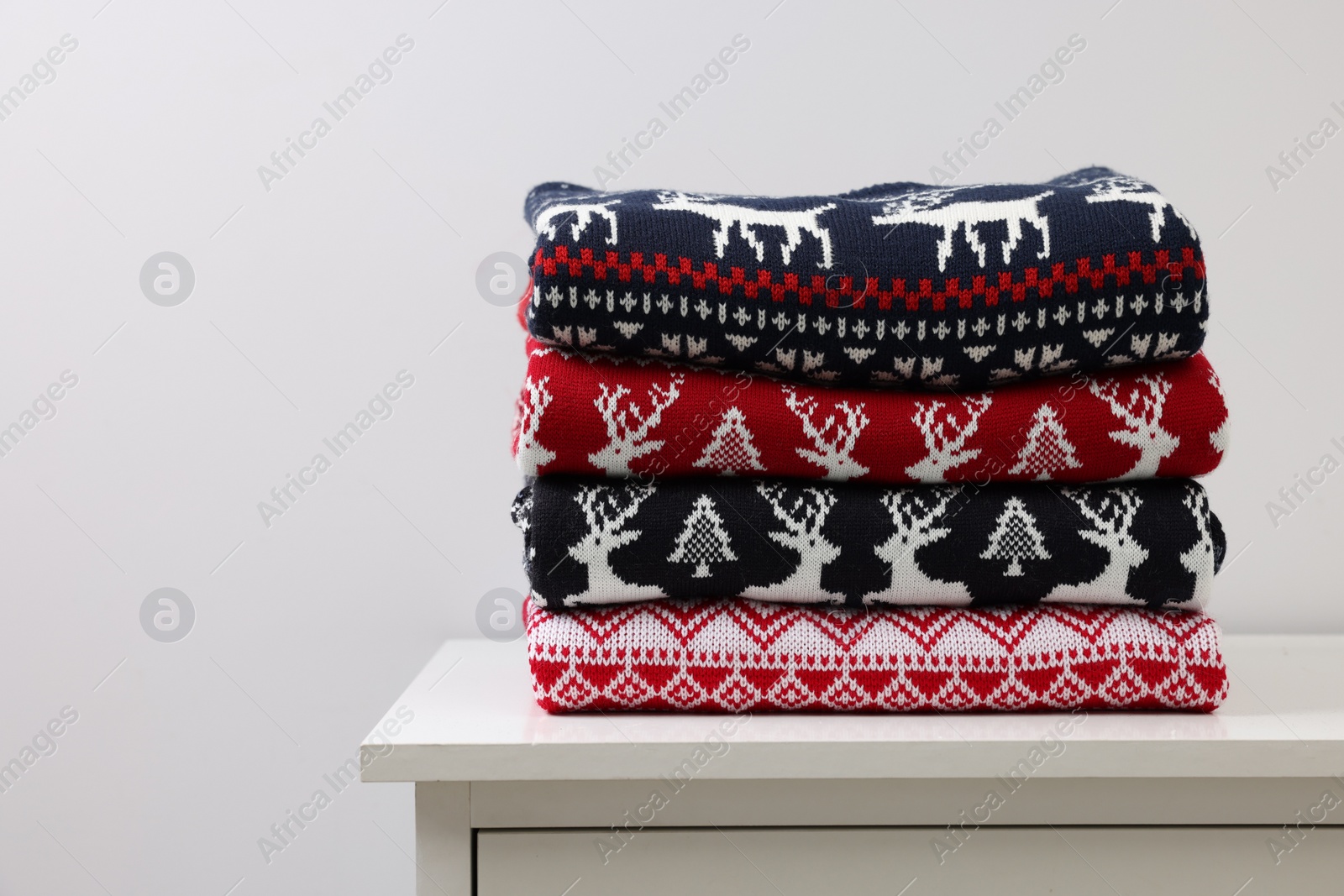 Photo of Different folded Christmas sweaters on chest of drawers against light background. Space for text