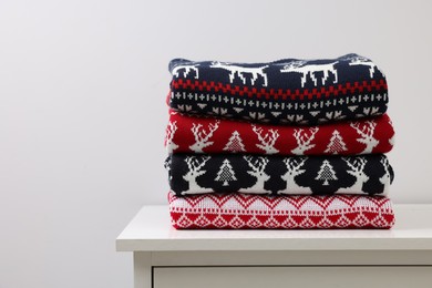 Different folded Christmas sweaters on chest of drawers against light background. Space for text