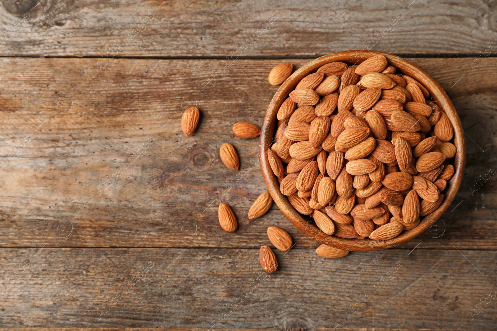 Photo of Tasty organic almond nuts in bowl and space for text on table, top view