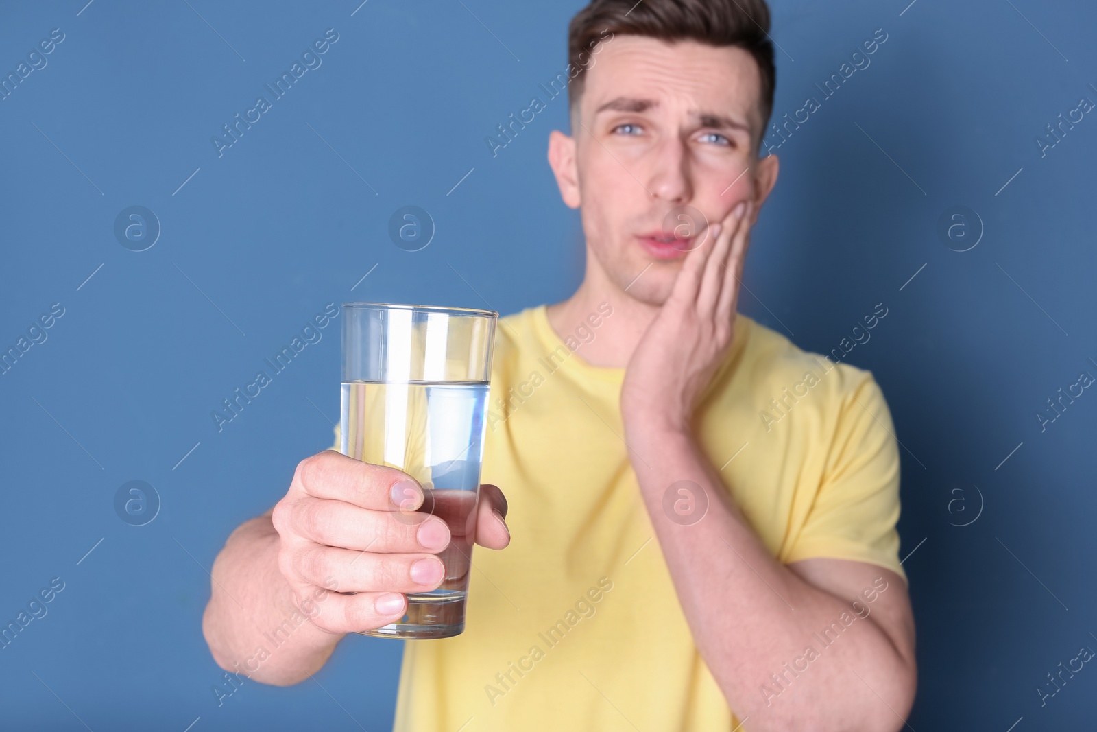 Photo of Young man with sensitive teeth and glass of cold water on color background