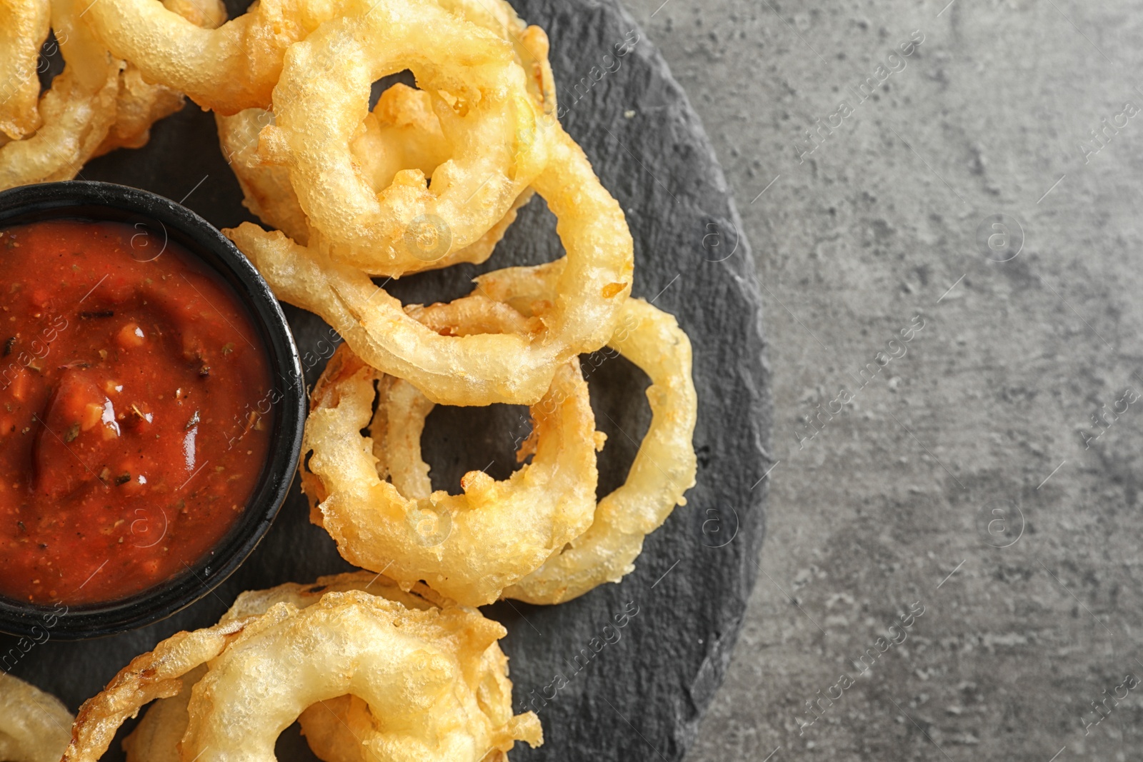 Photo of Delicious golden crispy onion rings and sauce on gray background, top view. Space for text