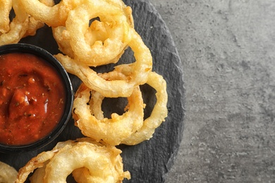 Photo of Delicious golden crispy onion rings and sauce on gray background, top view. Space for text