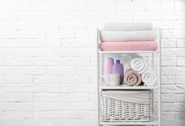 Photo of Shelving unit with clean towels and toiletries near brick wall. Space for text