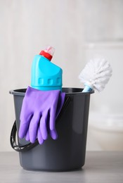 Bucket with bottle, toilet brush and gloves on table indoors. Cleaning supplies