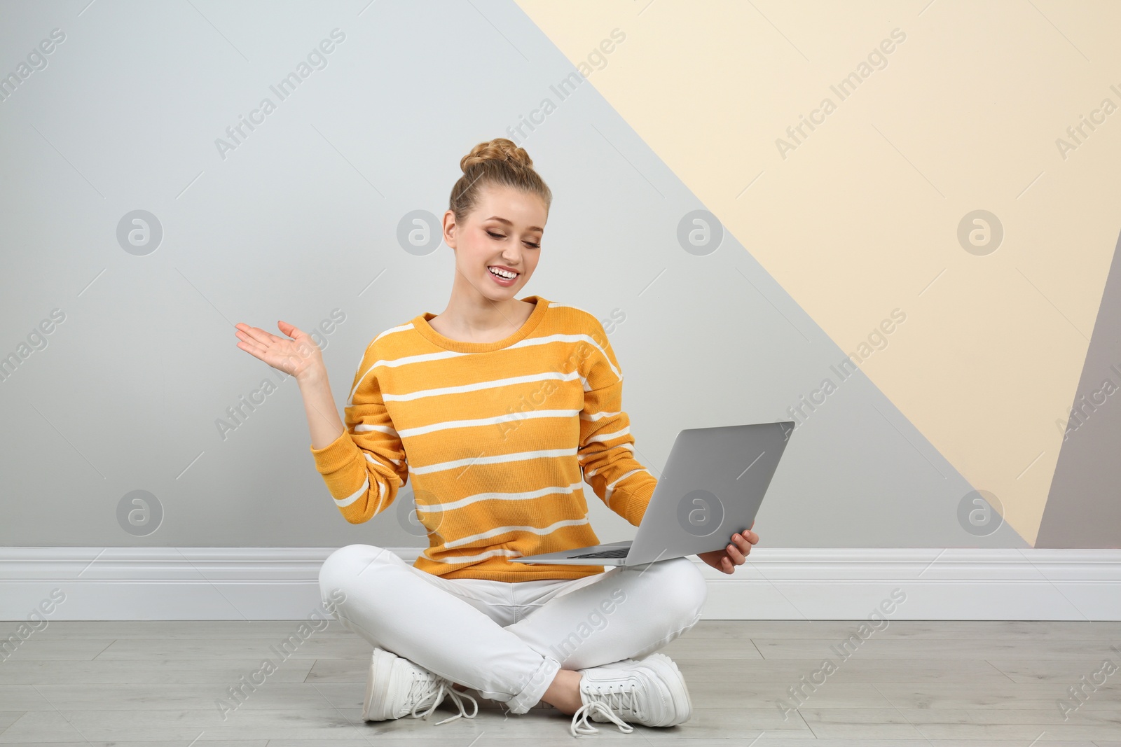 Photo of Young woman using laptop on floor near color wall