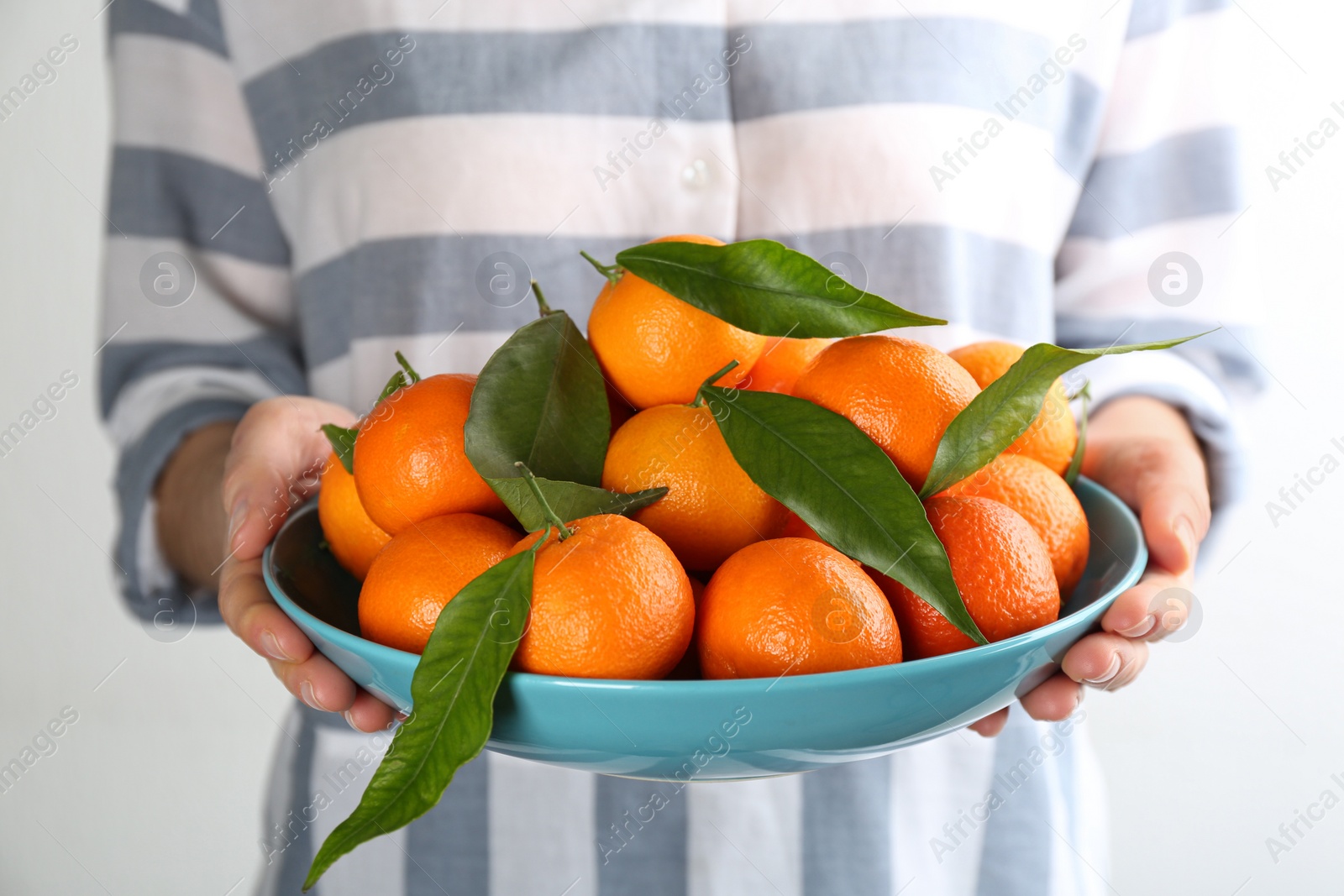 Photo of Woman holding plate with fresh tangerines on light background, closeup