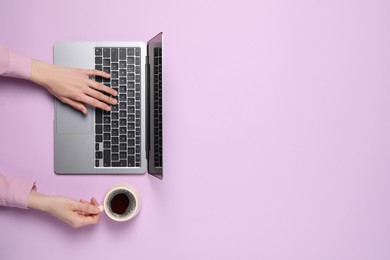 Photo of Woman with cup of coffee using laptop at lilac table, top view. Space for text