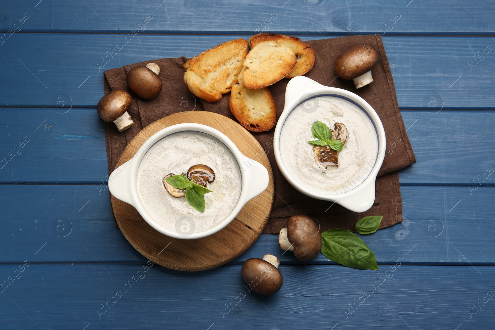 Photo of Delicious mushroom soup in ceramic pots and fresh ingredients on blue wooden table, flat lay