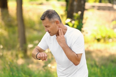 Photo of Man checking pulse outdoors on sunny day