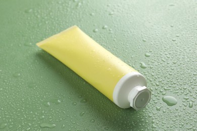 Photo of Moisturizing cream in tube on green background with water drops, closeup