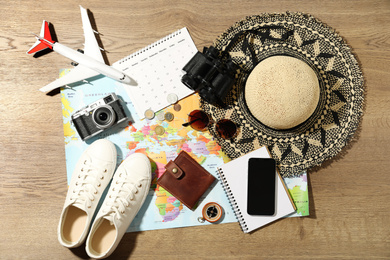 World map and items on wooden background, flat lay. Travel during summer vacation